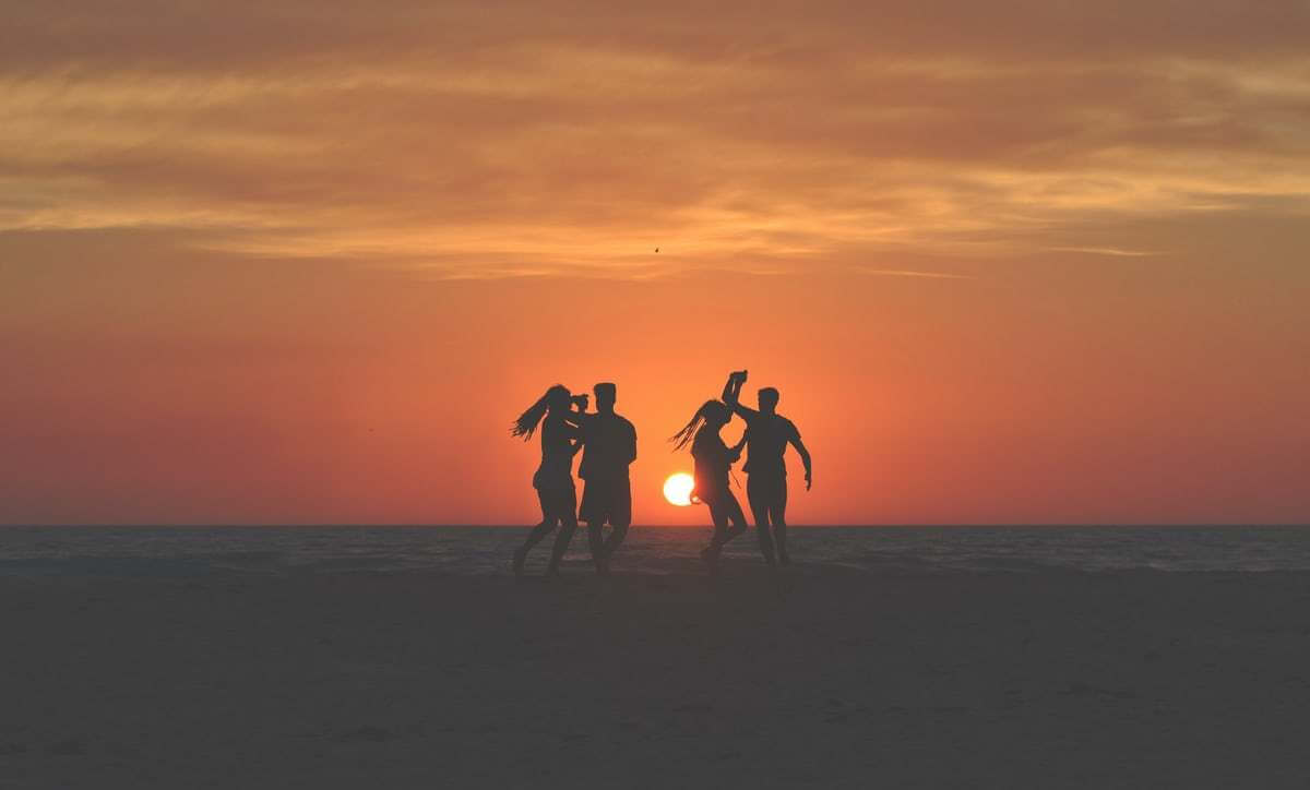 silhouette of four people dancing on beach
